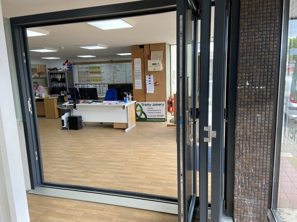 aluminium bi fold doors with slimline frames finished in anthracite grey interior showroom view bifold doors trinity windows jersey 2500